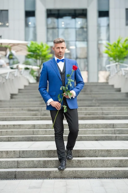 Mężczyzna w smokingu trzymający czerwoną różę