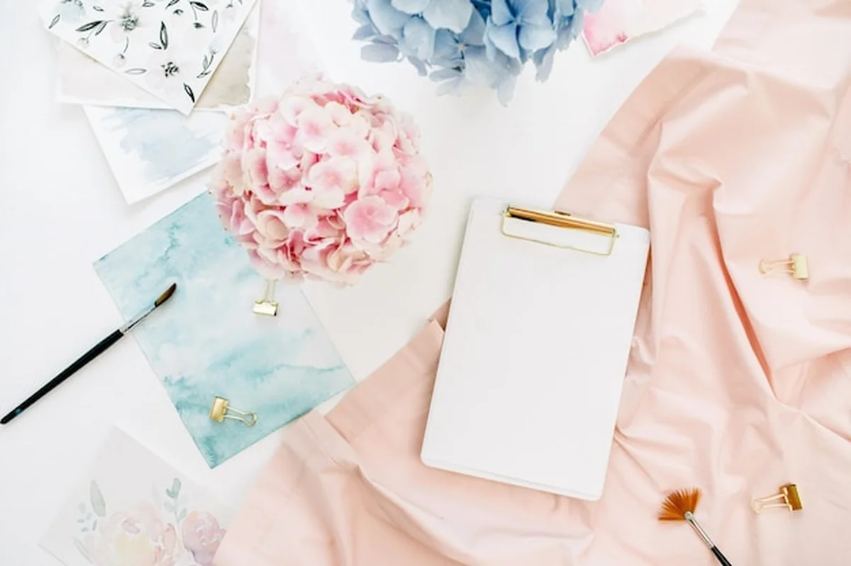 Kompozycja artystyczna na biurku z kwiatami hortensji, akwarelą i brzoskwiniowym kocem